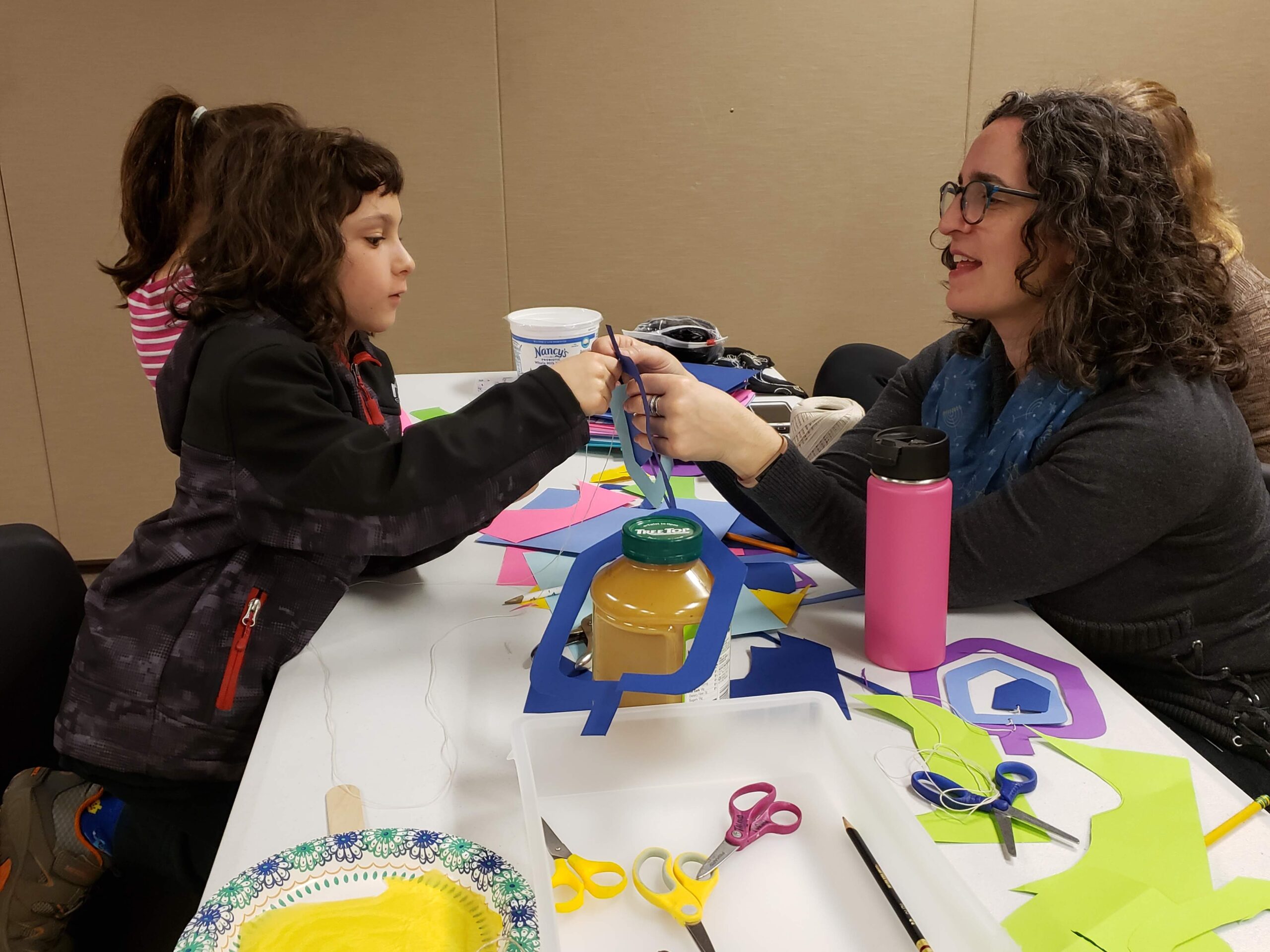 A woman and child sitting at a table with paper cut outs.