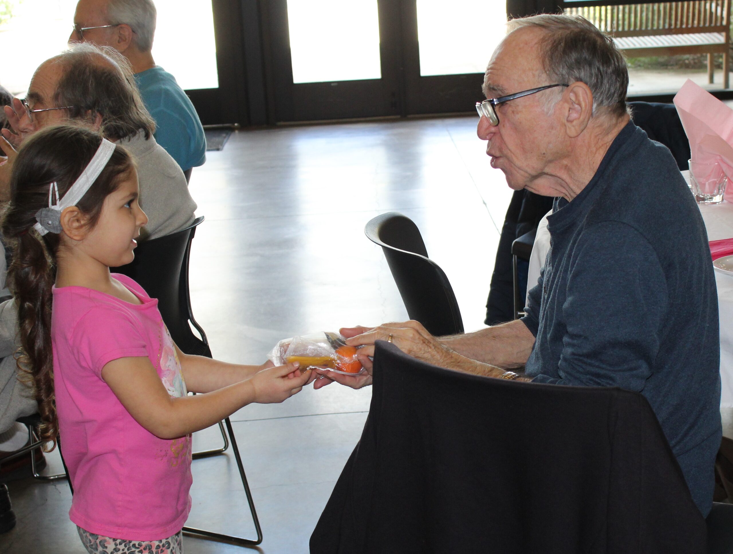 A little girl handing an old man some food.