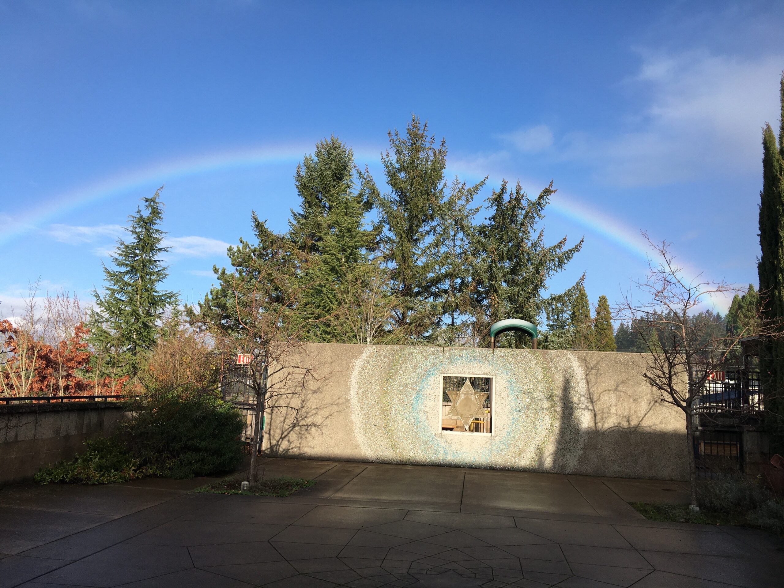 A rainbow is seen in the sky over a driveway.