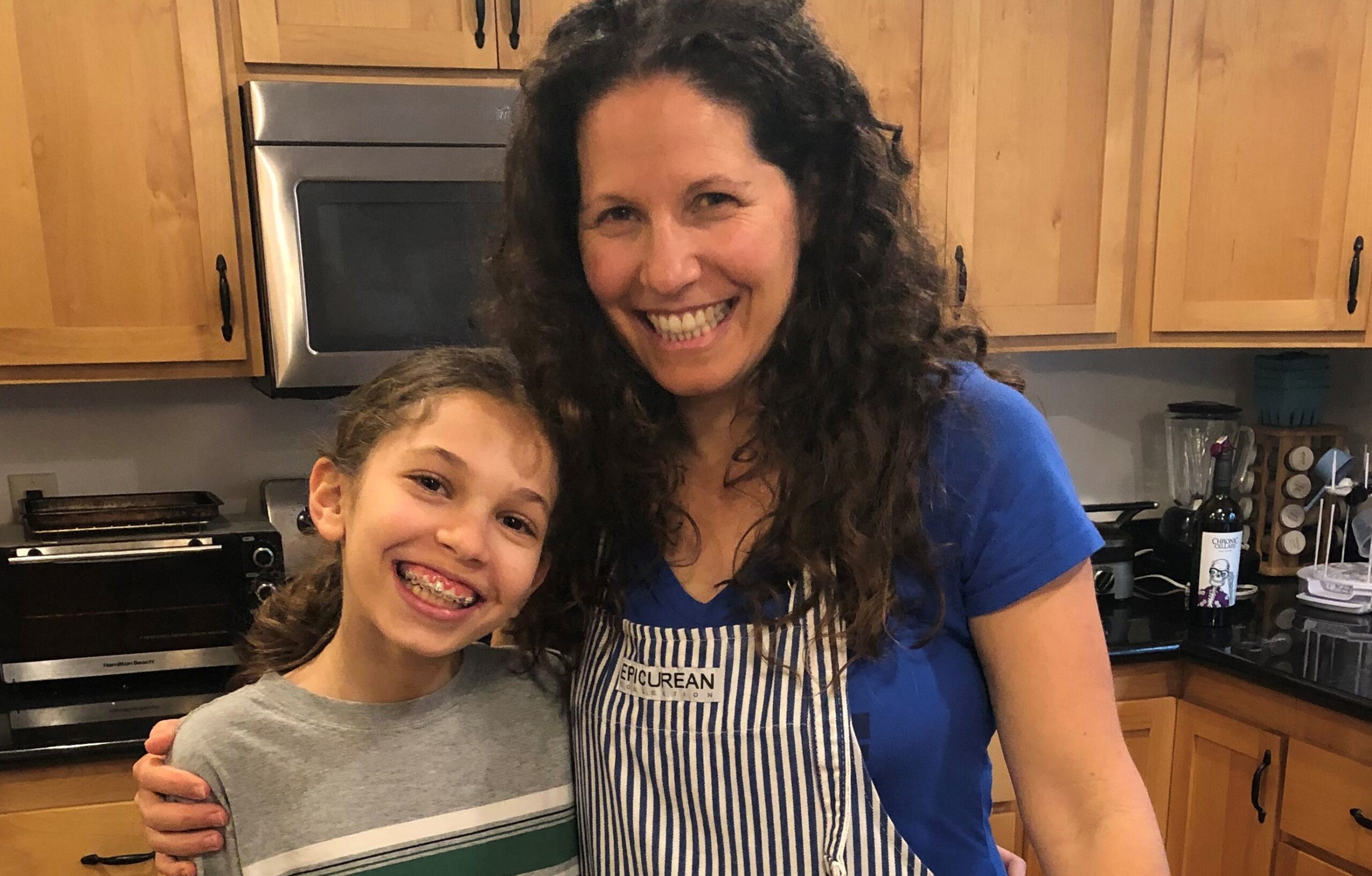 A woman and girl in the kitchen smiling for a picture.