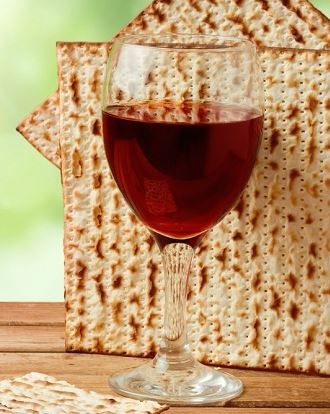 A glass of wine and matzah on a wooden table.
