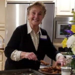 A woman smiles while preparing food in a kitchen.