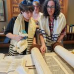 Three people in jewish garb looking at a torah scroll.