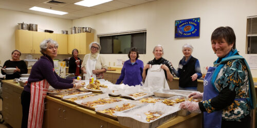 A group of people standing around a table with trays of food.