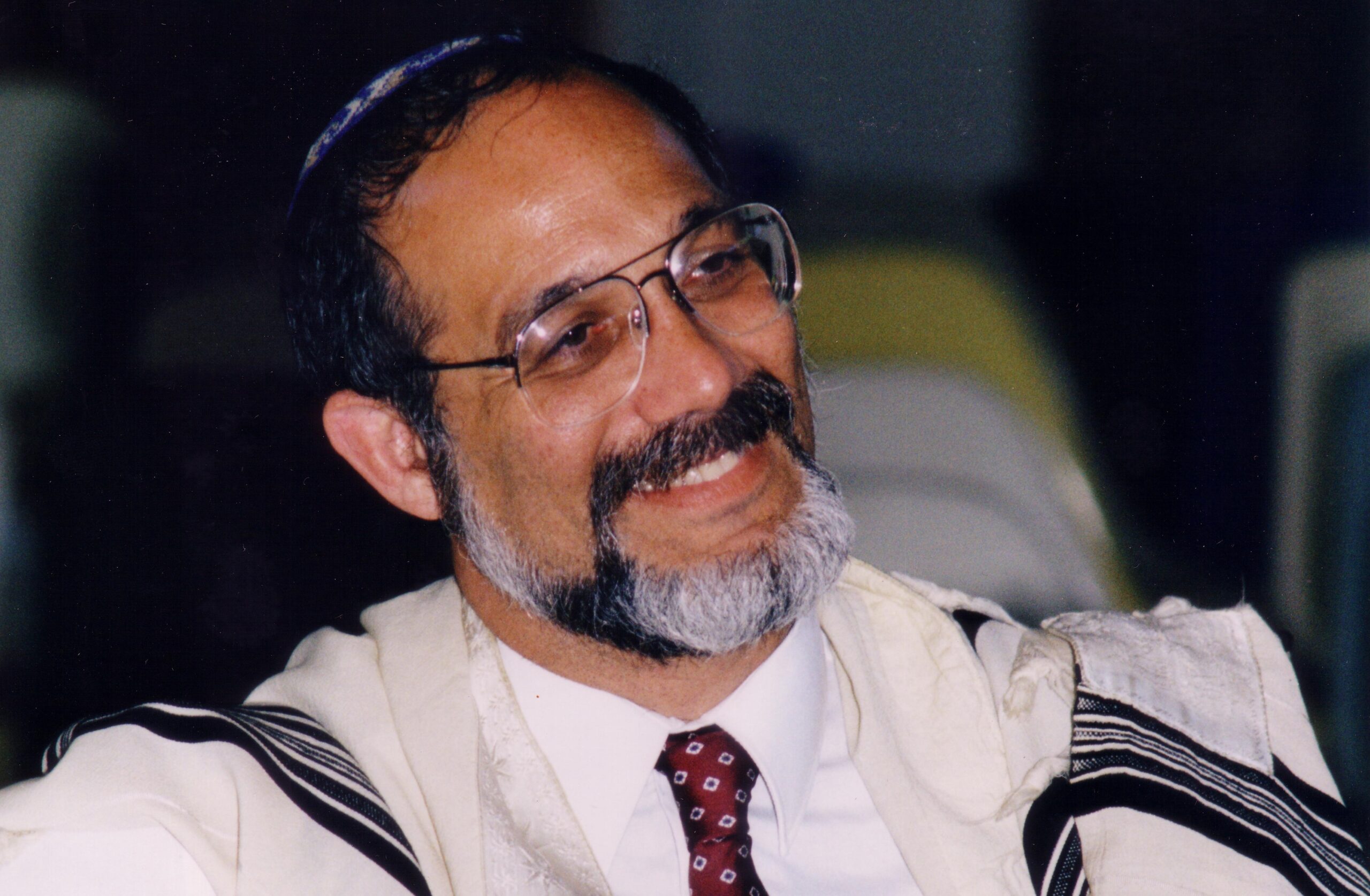 A man in glasses and a tie is smiling.