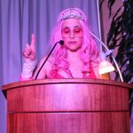 A woman with pink hair is speaking at a podium.