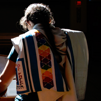 A woman wearing a colorful tallit and holding her hair back.