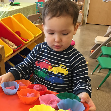 A toddler playing with colorful cups in the classroom.