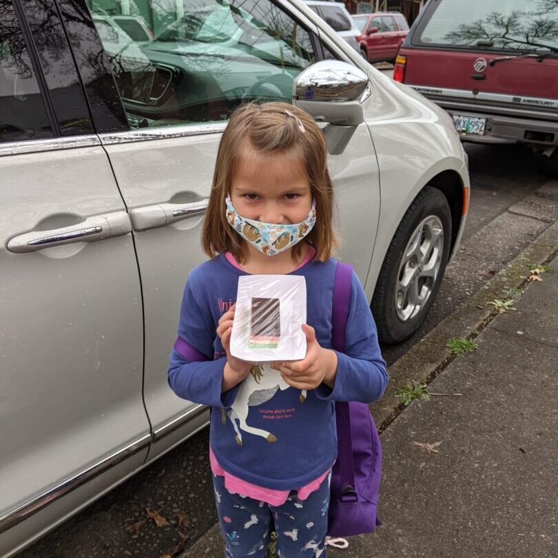 A little girl holding a box in front of her car.