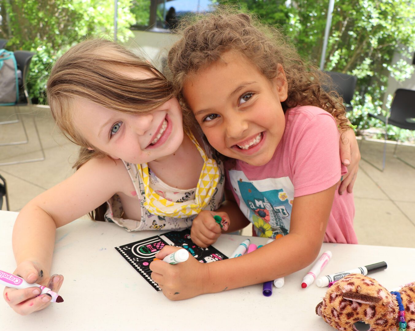 Two young girls sitting at a table with markers and crayons.