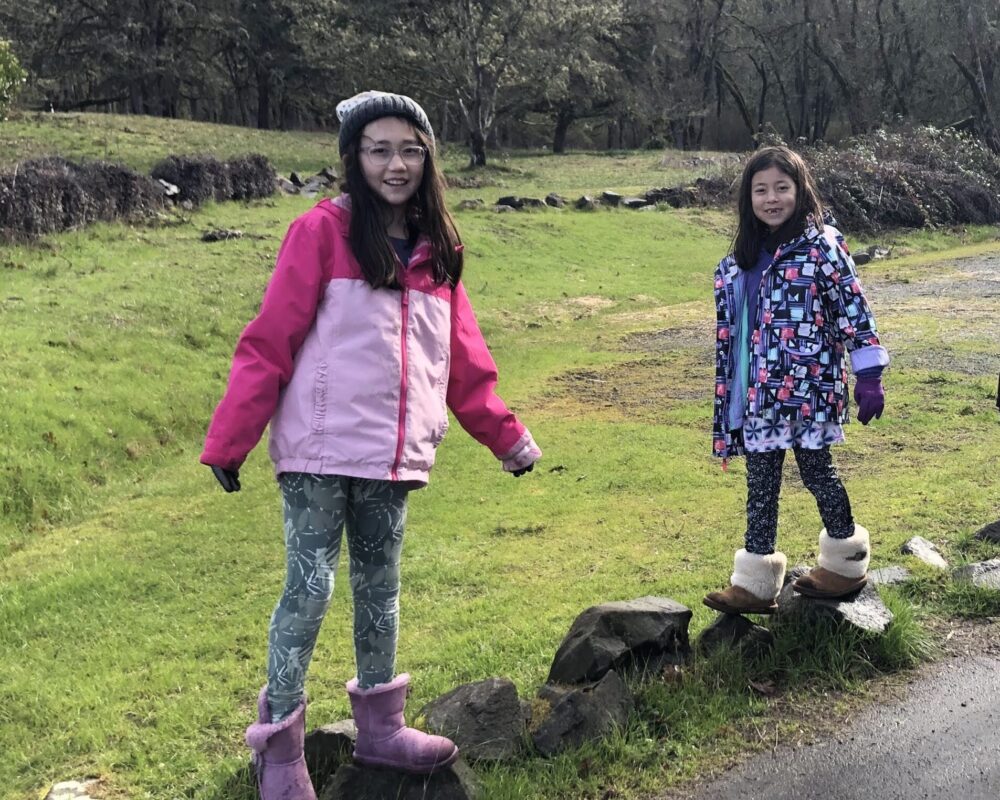 Two girls standing on a hill near the road.